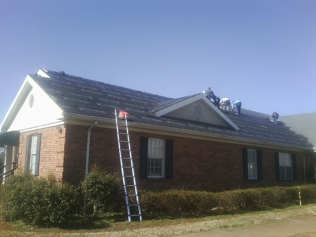 Crew tearing shingles off a brick ranch roof with a ladder set — Metal Roof Repair work by our crew in Shrewsbury