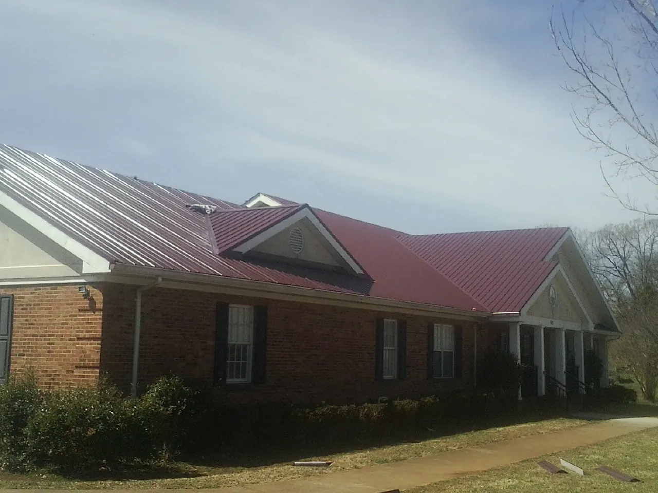Red metal roof with gabled entries on a long brick building, from a Hail Damage Roof Repair job in Shrewsbury