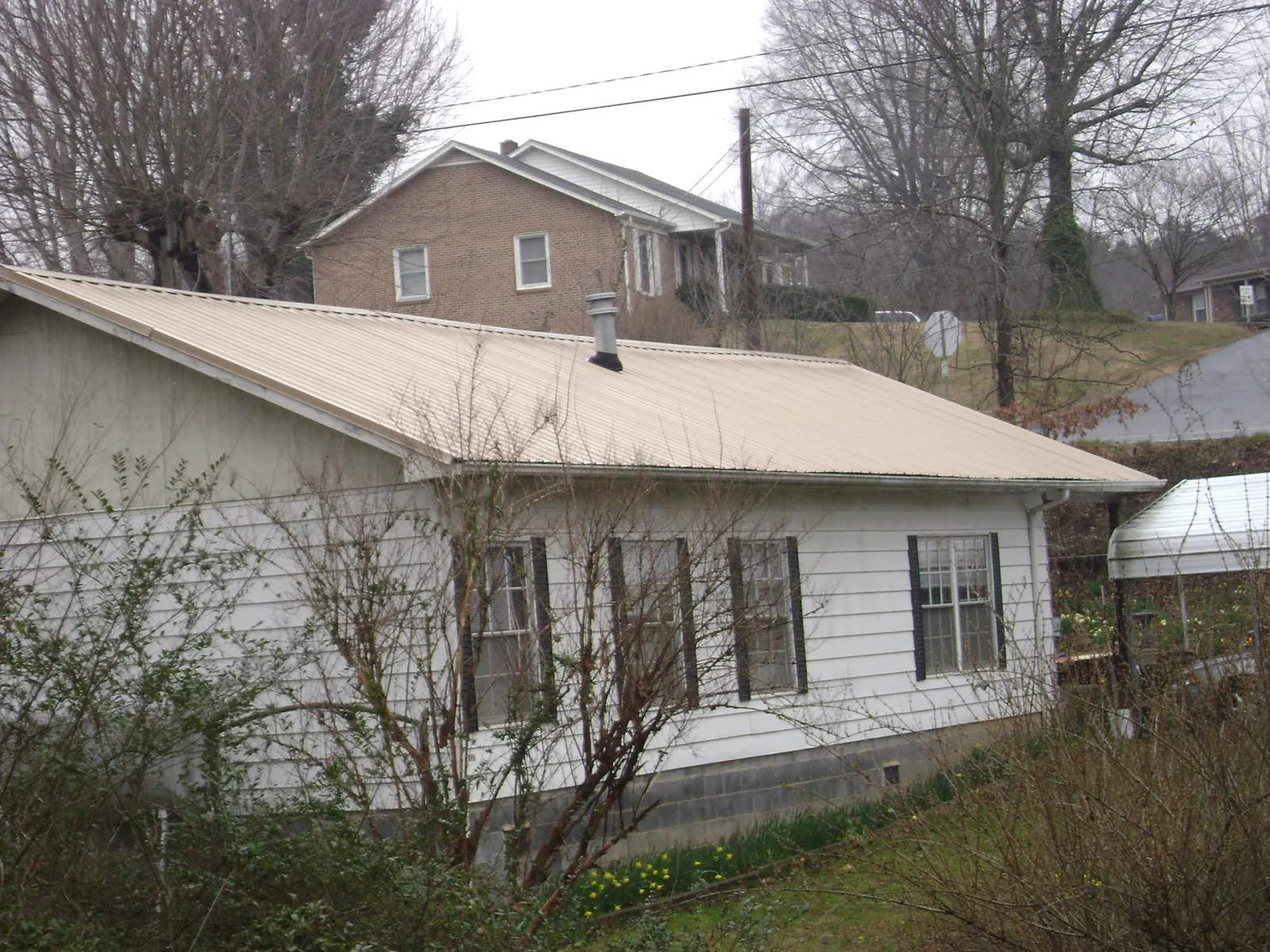 Tan metal roof on a white sided house set into a hillside — Commercial Roofing by Roofing Brothers in Shrewsbury